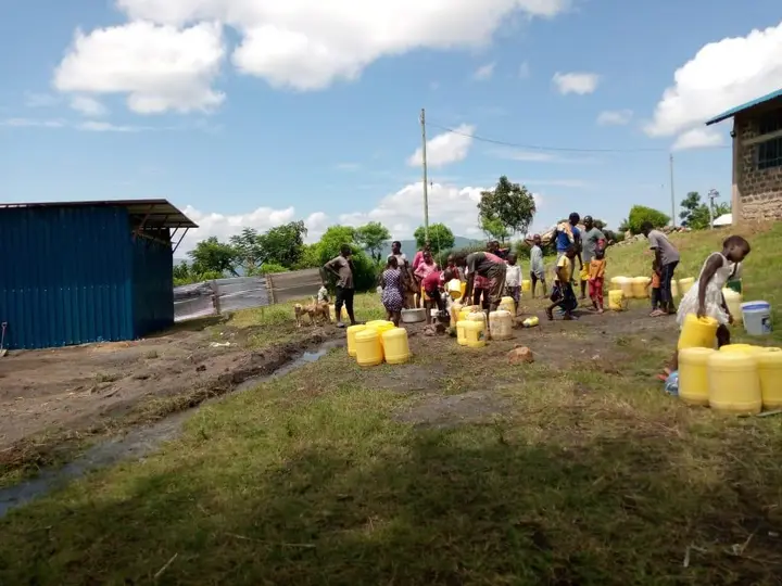 People gathered around a water outlet with yellow containers at the Isiolo site.