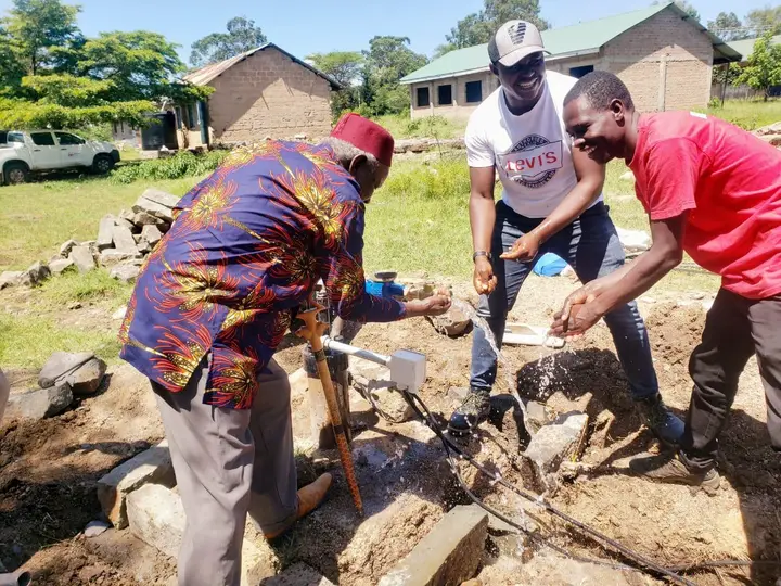 Three people beside the water outlet, with water flowing into their hands.
